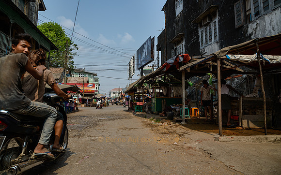 Ein Mopedfahrer braust mit Passagier durch die Strassen von Mawlamyaing