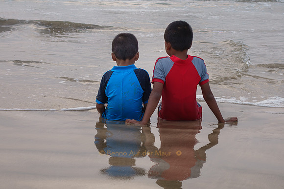 Zwei kleine Buben sitzen am Strand und schauen aufs Meer