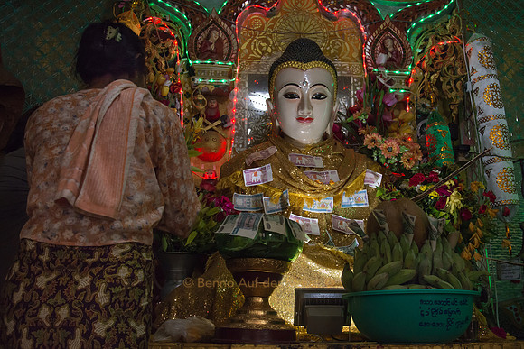 Eine ältere Frau stellt Blumen bei einer Buddha-Statue hin