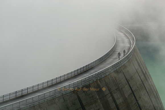 Fussgänger tauchen aus dem Nebel der Staumauer des Lac de Moiry auf