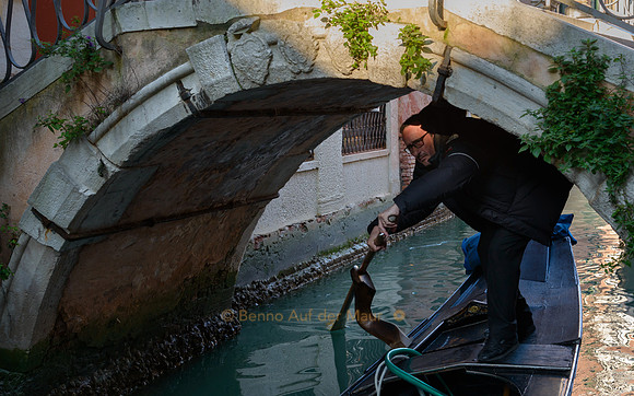 Ein Gondoliere duckt sich unter einer kleinen Brücke